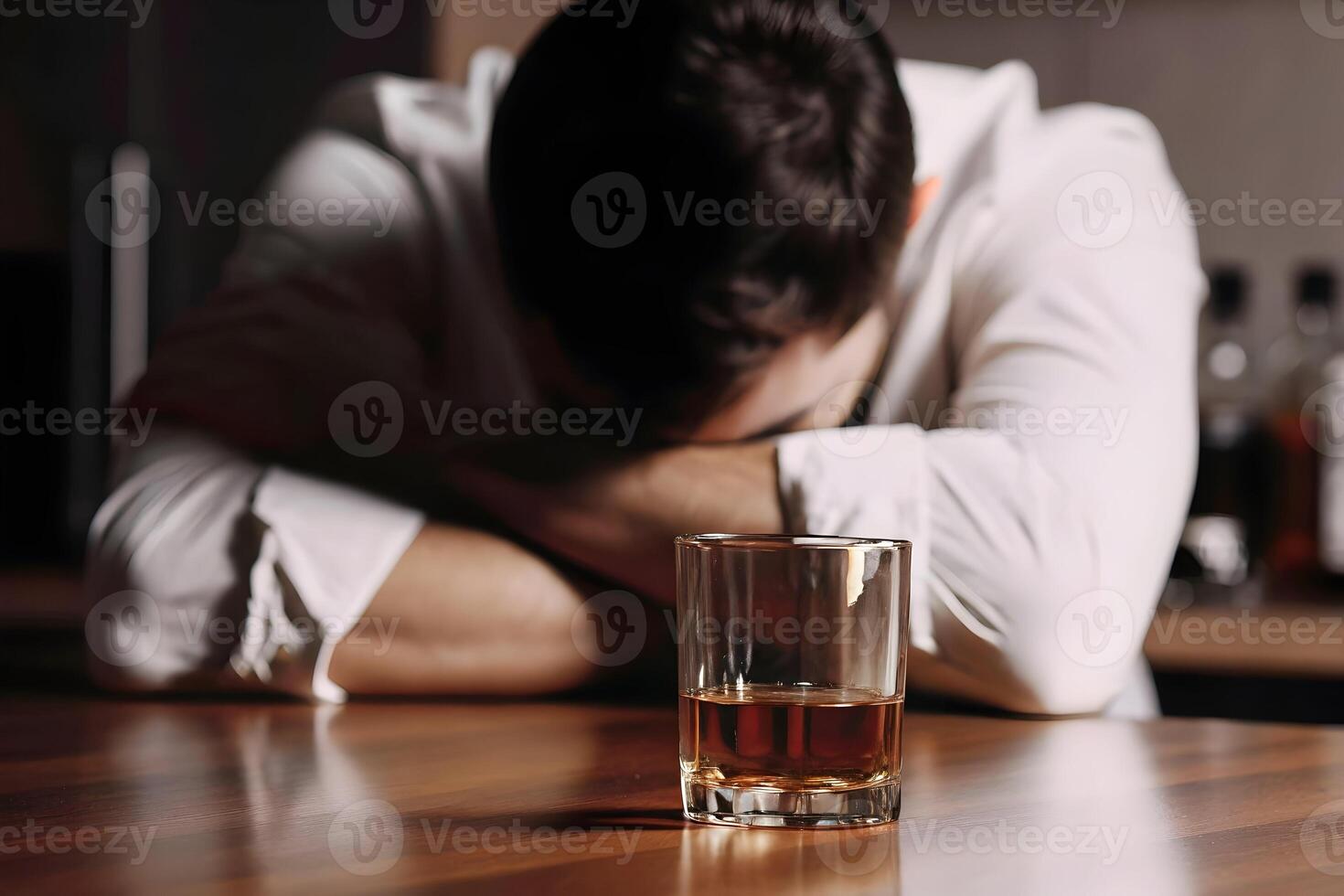 Man slumped over a table with a half-full glass of alcohol photo