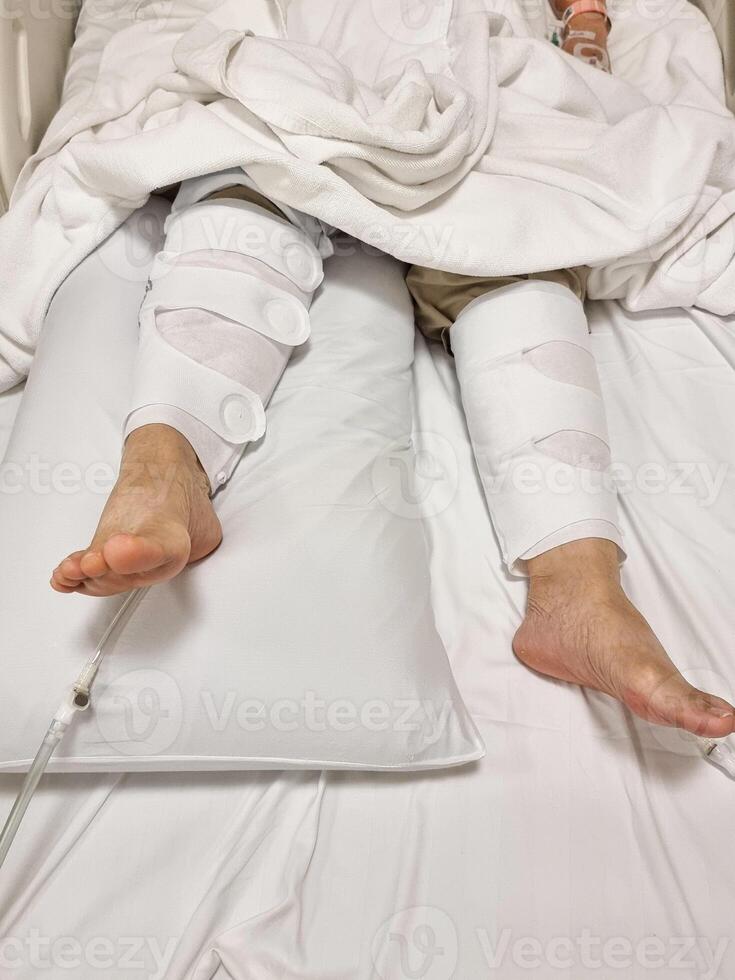 A patient lying on a bed with both legs wrapped in a blood circulation device, used after knee replacement surgery in the hospital. photo