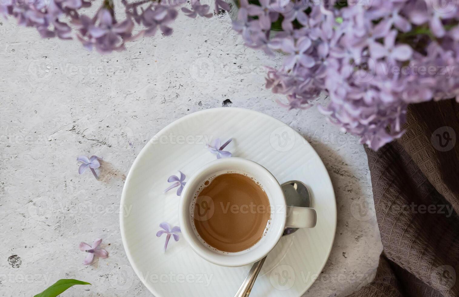The postcard is beautiful. A fancy purple coffee mug, an old book, a straw hat and a bouquet of purple lilac. Beautiful still life. Spring time. The concept of Good morning. photo