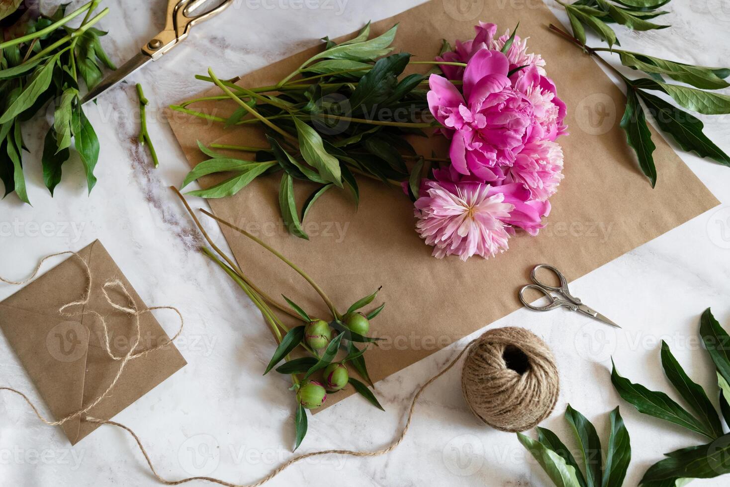 A close-up view of hands delicately handling pink peonies on craft paper, with tools and materials scattered around. photo