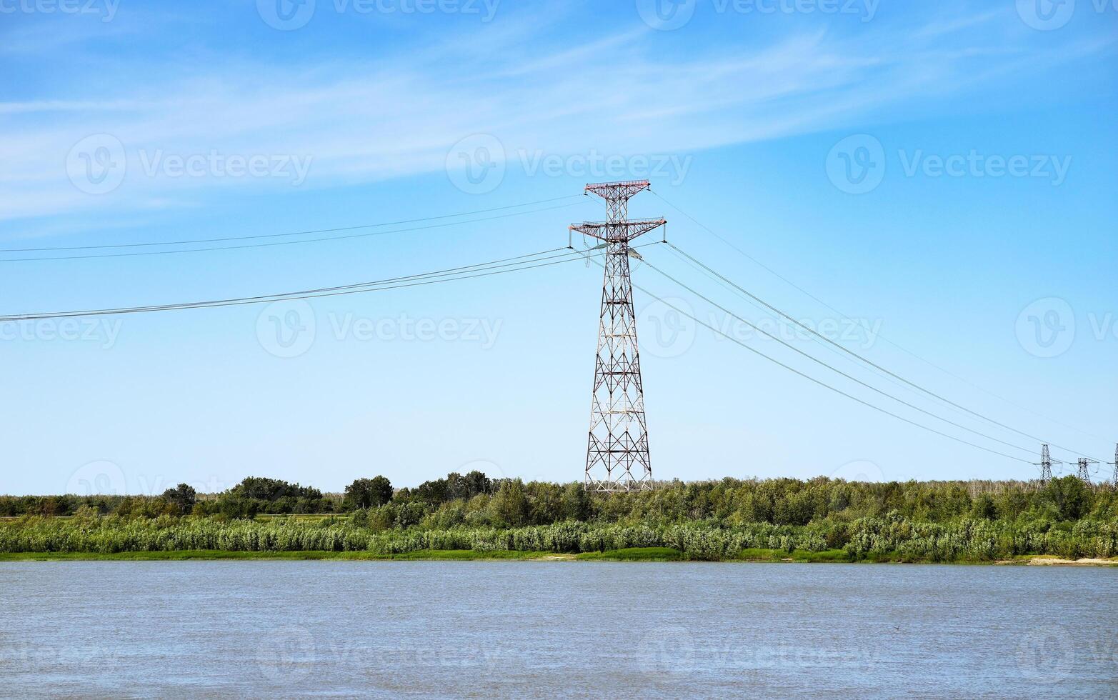 High voltage lines and power pylons in a flat and green agricultural landscape on a sunny day with cirrus clouds in the blue sky. photo