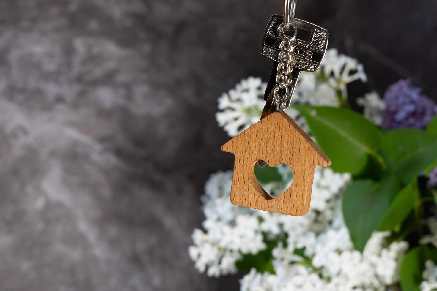 Close-up of the keys and keychain in the form of a house against a background of lilac, a symbol of the family hearth and own home. Purchase of real estate. photo