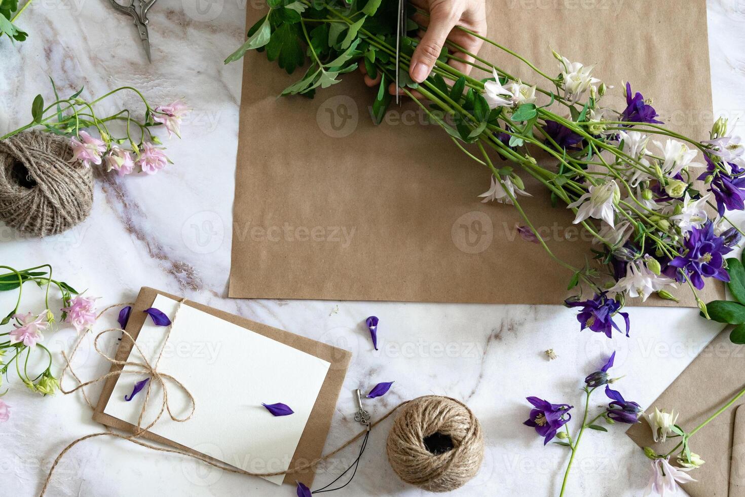 Closeup of hands of young woman florist creating invitation, put in envelope blossom flowers, top view. Macro. Isolated on white background. With free space for your text photo