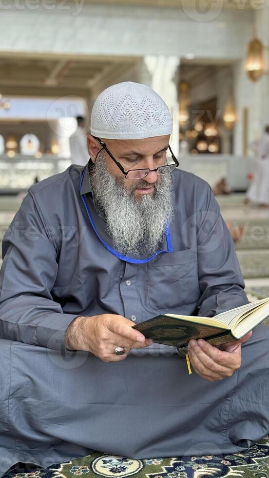 Mecca, Saudi Arabia - May 2, 2024. Young man, Hajj and Umrah pilgrim sitting and reading Quran in Masjidil Haram, Great Mosque in Makkah, Saudi Arabia. Hajj 2024. photo