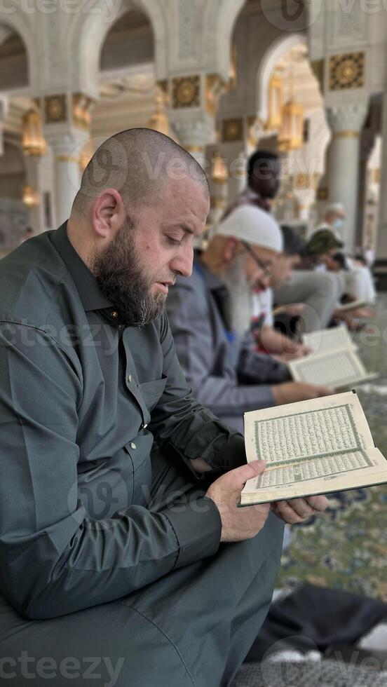 Mecca, Saudi Arabia - May 2, 2024. Young man, Hajj and Umrah pilgrim sitting and reading Quran in Masjidil Haram, Great Mosque in Makkah, Saudi Arabia. Hajj 2024. photo