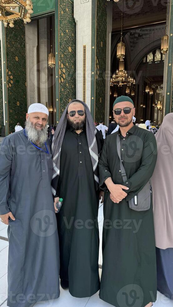 Three Muslim men in Ihram clothing standing in front of the Kaaba during Hajj or Umrah pilgrimage in Mecca, Saudi Arabia. Sacred Islamic journey at Masjid al-Haram photo