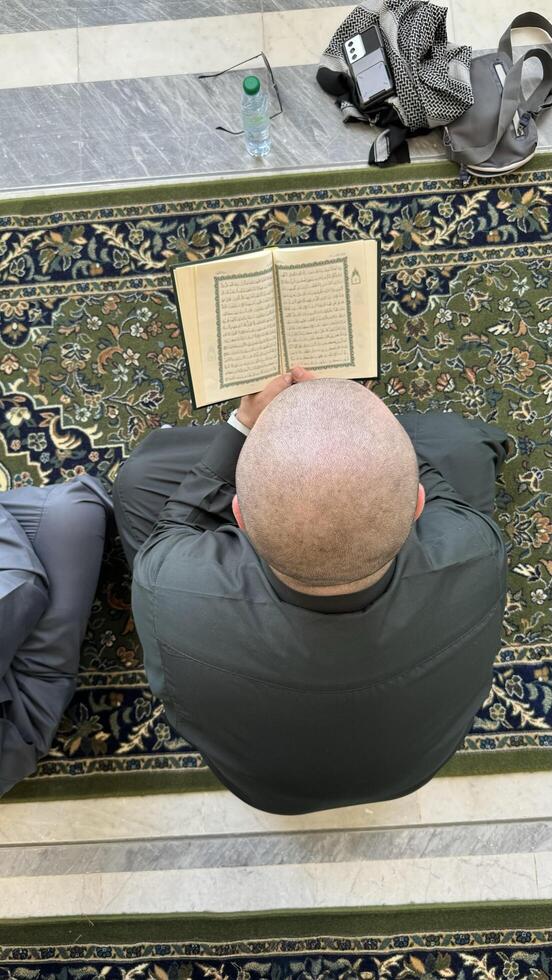 Mecca, Saudi Arabia - May 2, 2024. Young man, Hajj and Umrah pilgrim sitting and reading Quran in Masjidil Haram, Great Mosque in Makkah, Saudi Arabia. Hajj 2024. photo