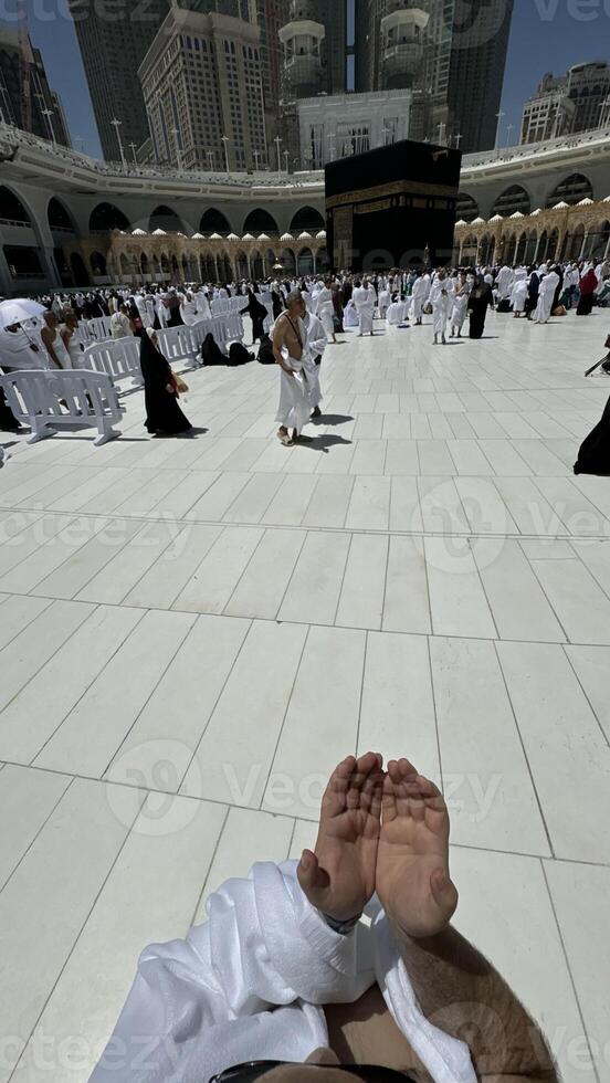 A bald man poses for a photo in front of the Kaaba at noon after performing Umrah at Masjid al-Haram, Mecca. A sacred Islamic pilgrimage in the heart of the holy mosque under the bright sunlight.