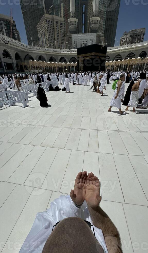 A bald man poses for a photo in front of the Kaaba at noon after performing Umrah at Masjid al-Haram, Mecca. A sacred Islamic pilgrimage in the heart of the holy mosque under the bright sunlight.