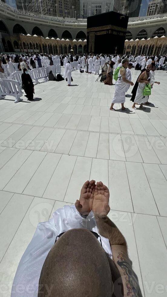 A bald man poses for a photo in front of the Kaaba at noon after performing Umrah at Masjid al-Haram, Mecca. A sacred Islamic pilgrimage in the heart of the holy mosque under the bright sunlight.