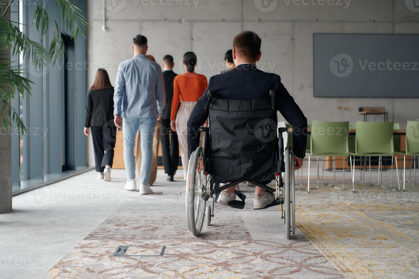 A diverse team of business professionals in a modern office stands alongside their director in a wheelchair, embodying inclusivity, collaboration, and leadership in the workplace photo
