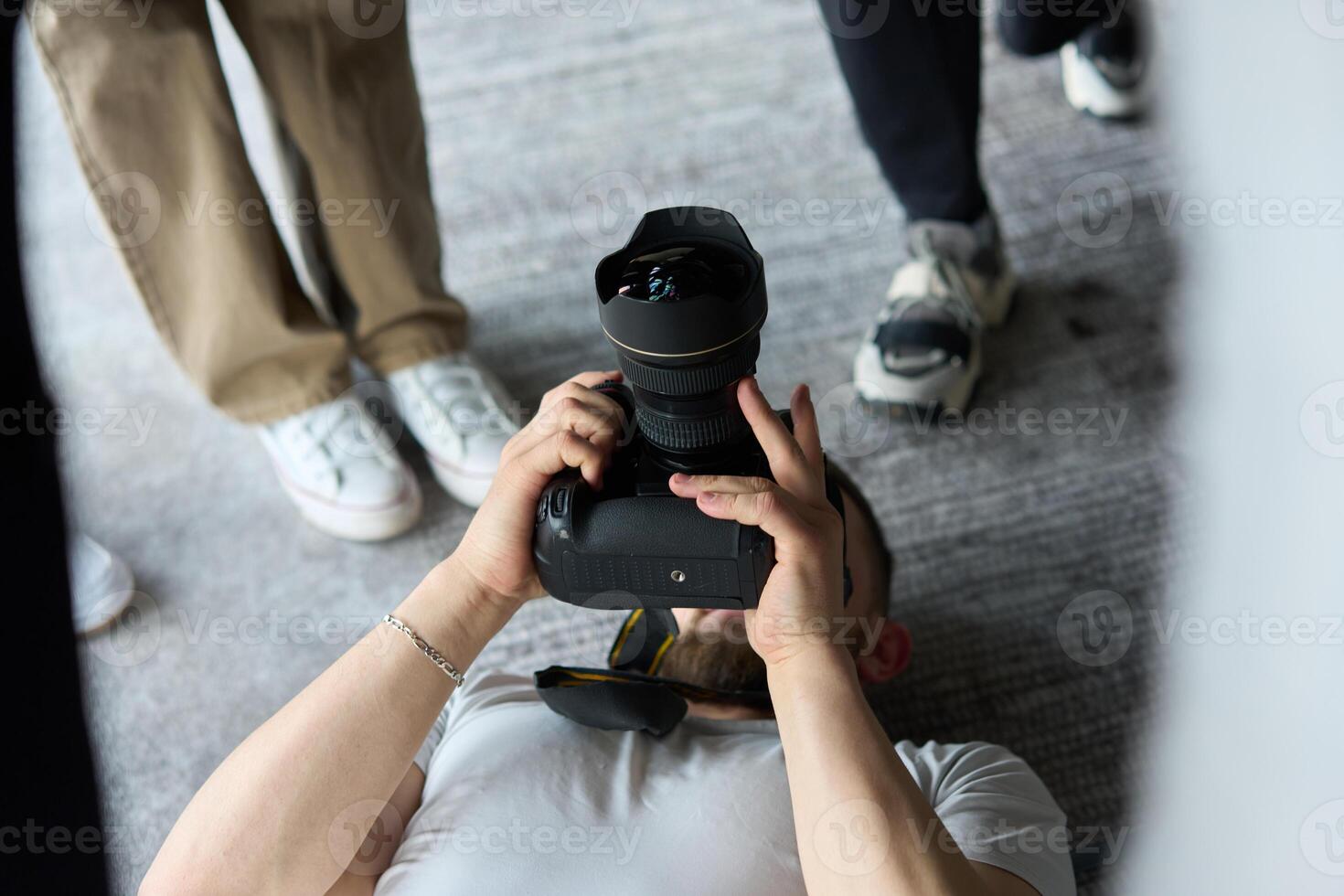 A photographer lies on the floor, capturing a heartfelt shot of a group of models embracing each other, showcasing their natural connection and joy in an intimate and creative moment photo