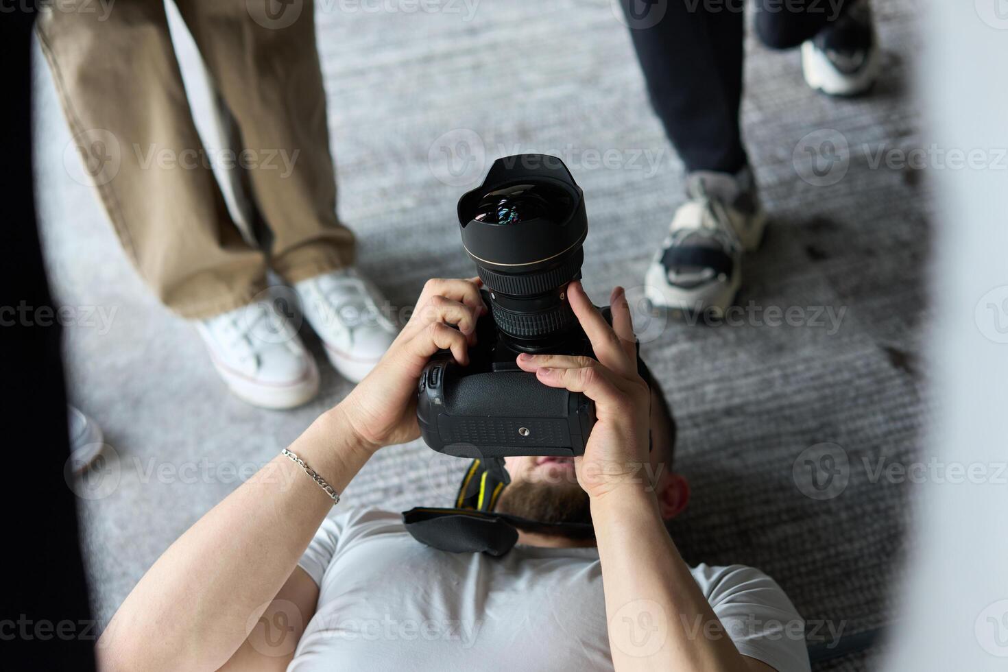 A photographer lies on the floor, capturing a heartfelt shot of a group of models embracing each other, showcasing their natural connection and joy in an intimate and creative moment photo