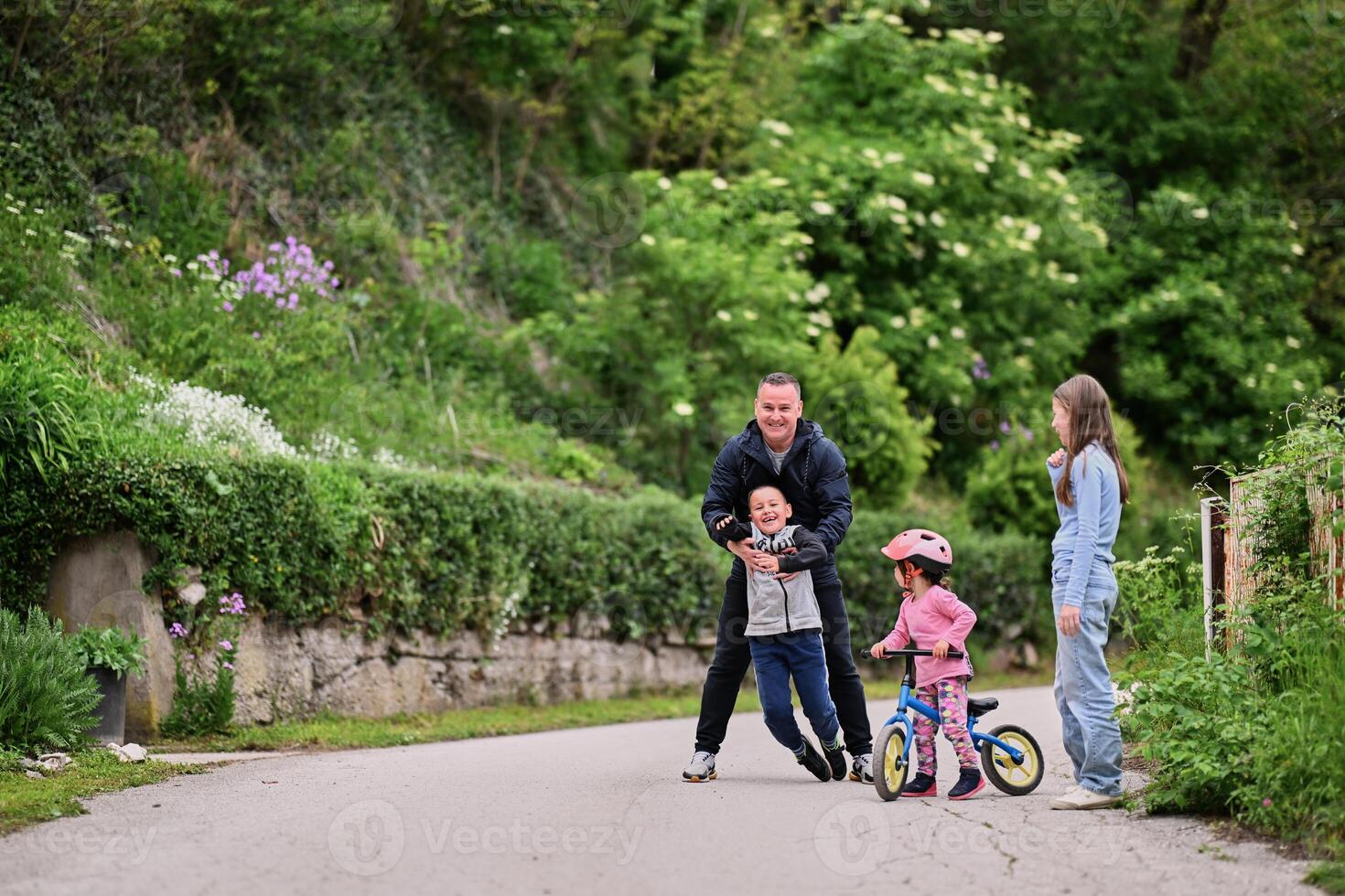 A group of children, including a boy and girl playing with a ball and their young friend riding a bike, enjoying a fun filled day in a natural outdoor setting photo