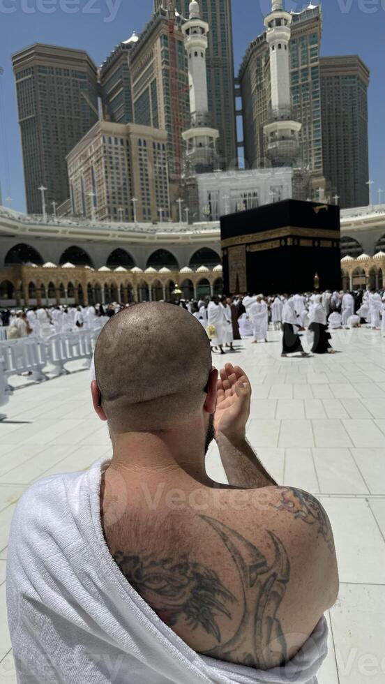 Former Sinner man who converted to Islam, with a large tattoo on his back and arm, praying with devotion in Makkah while gazing at the sacred Kaaba, embracing his new faith with deep spiritual photo