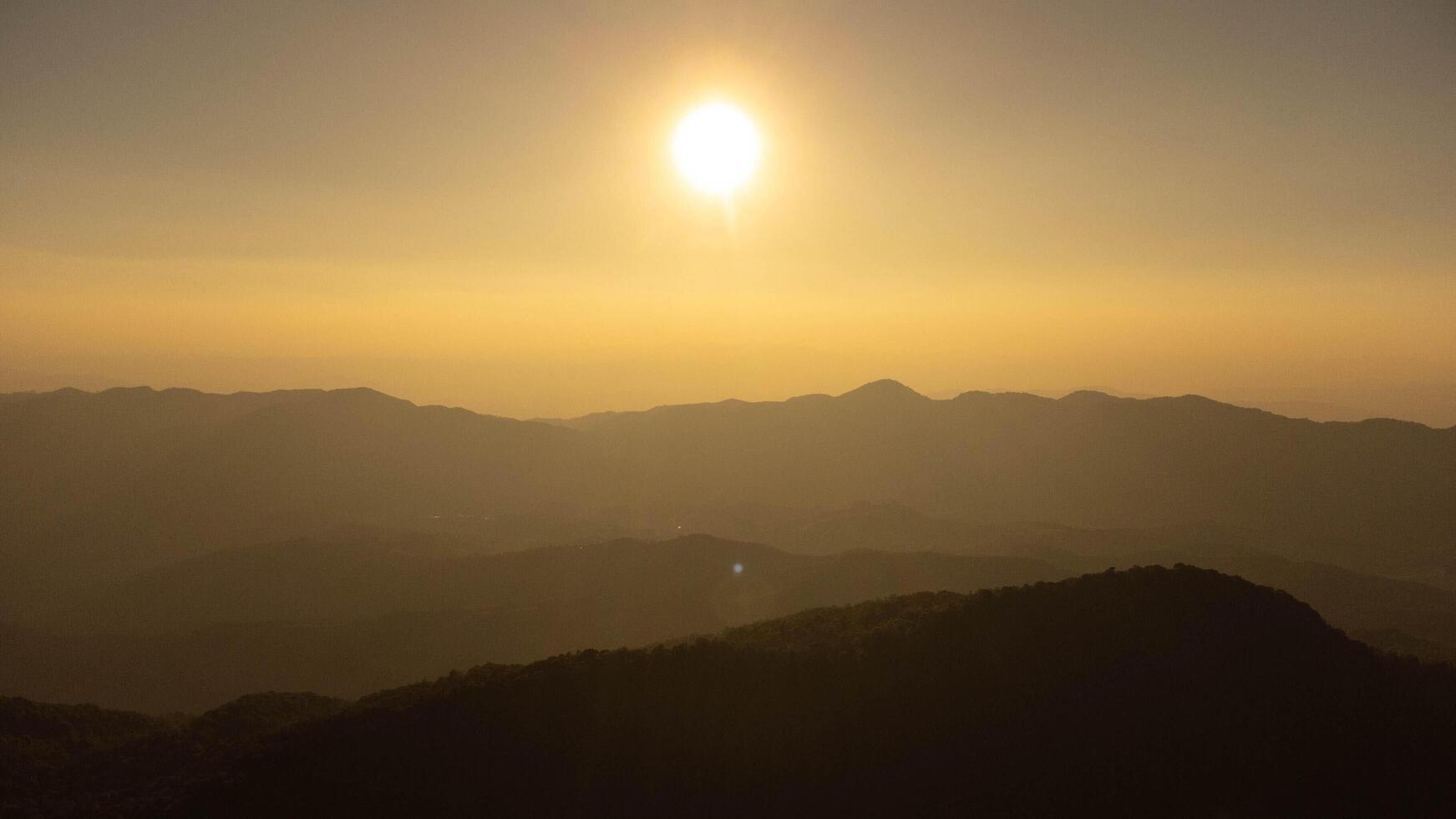 The setting sun shines down on a serene mountain landscape covered with tropical trees. photo