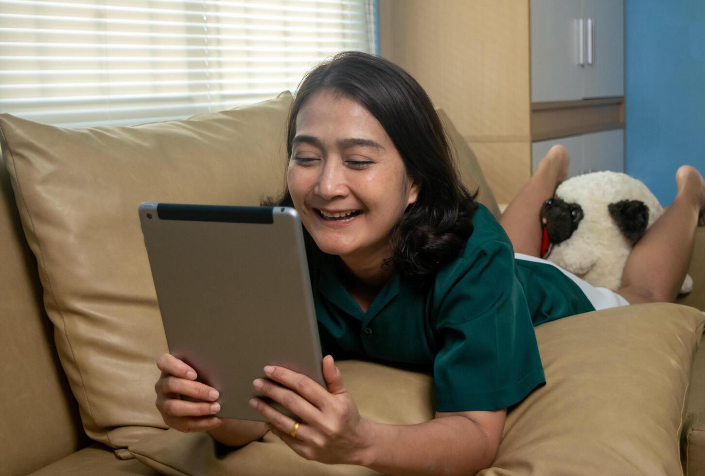 Asian women lying down on the sofa watching movies online digital tablet and laughing happiness, using social media, reading e-books online relaxing vacation lifestyles concepts at home photo