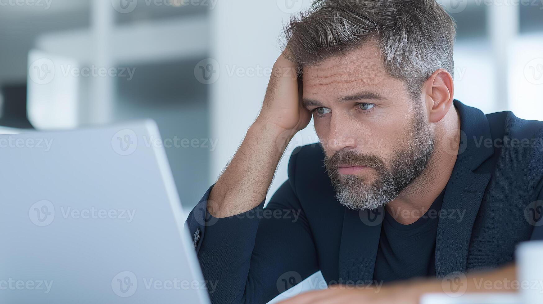 Stressed businessman in office looking at laptop screen, head resting on hand. Concept of tiredness, overload and work problems photo