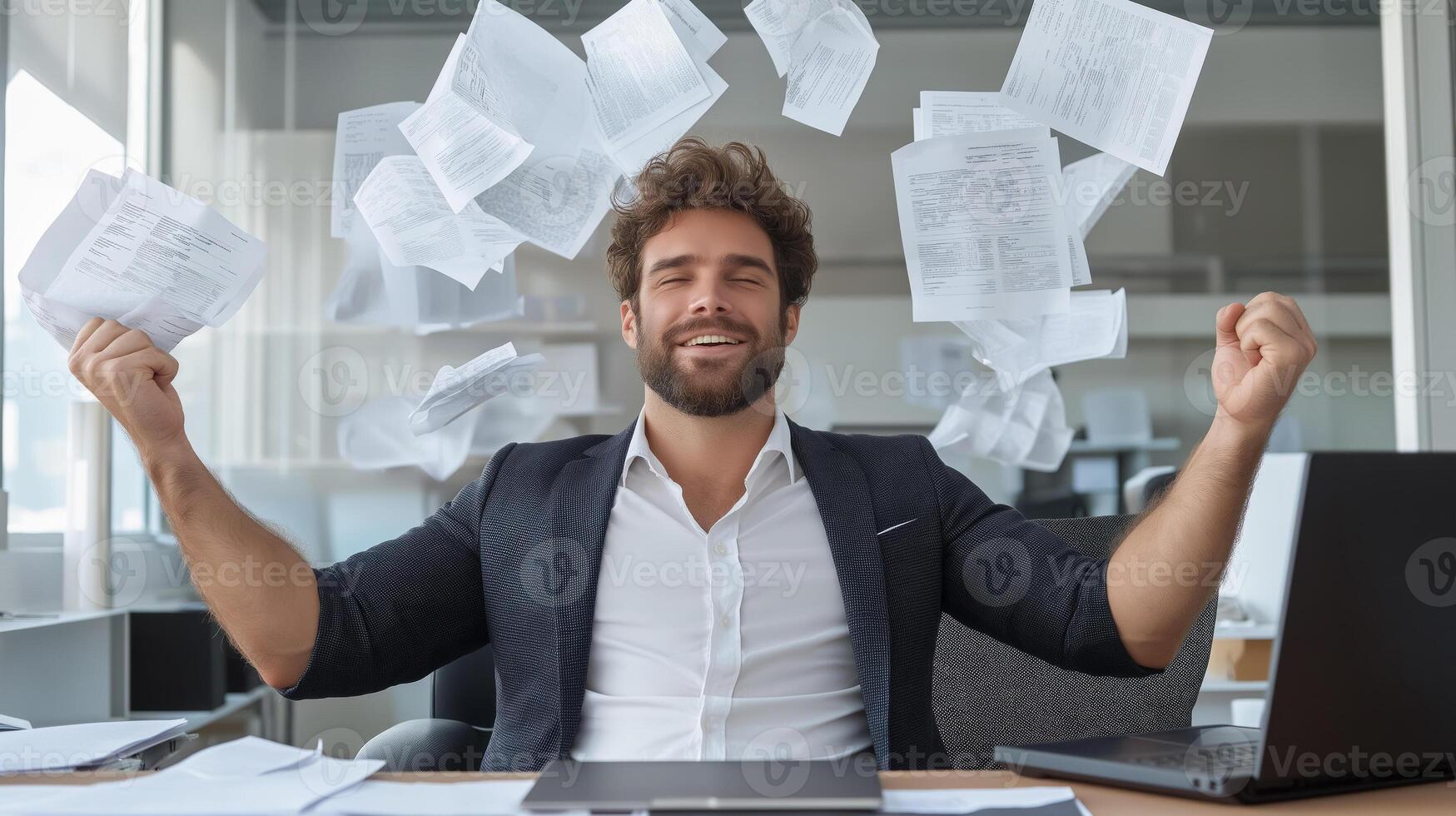 Contented man in a business suit leans back in his chair, raising his hands up, and documents fly around him. An atmosphere of happiness, success and liberation from work in a modern office. photo