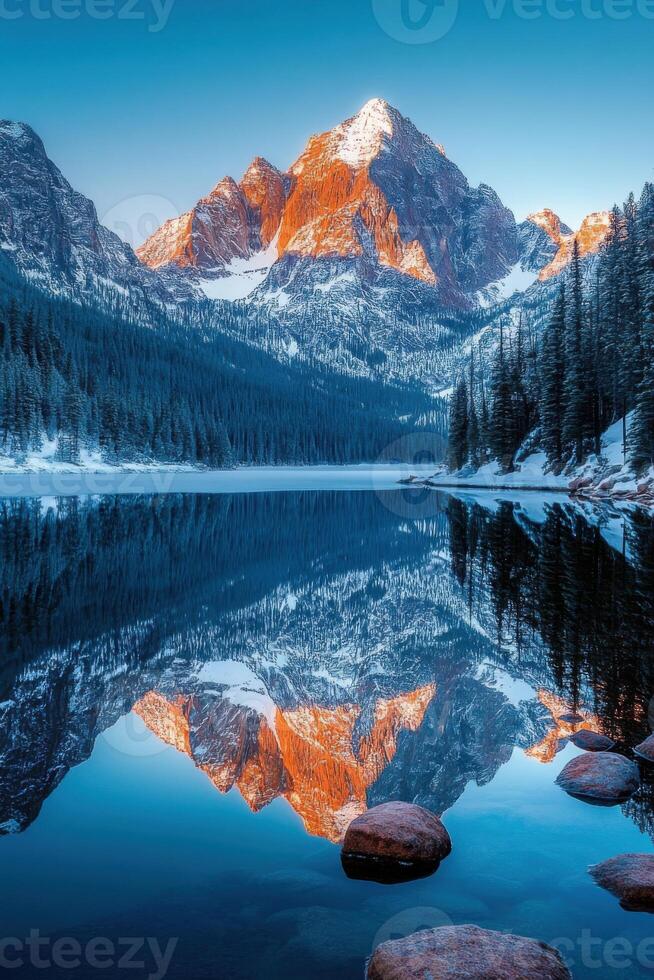 Snowy mountain reflects in a calm lake. Winter scene with rocks in the water. Trees line the shore of the still, peaceful lake. photo