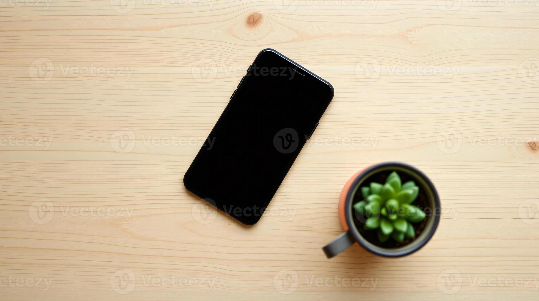 A black smartphone and a small plant on a wooden table photo