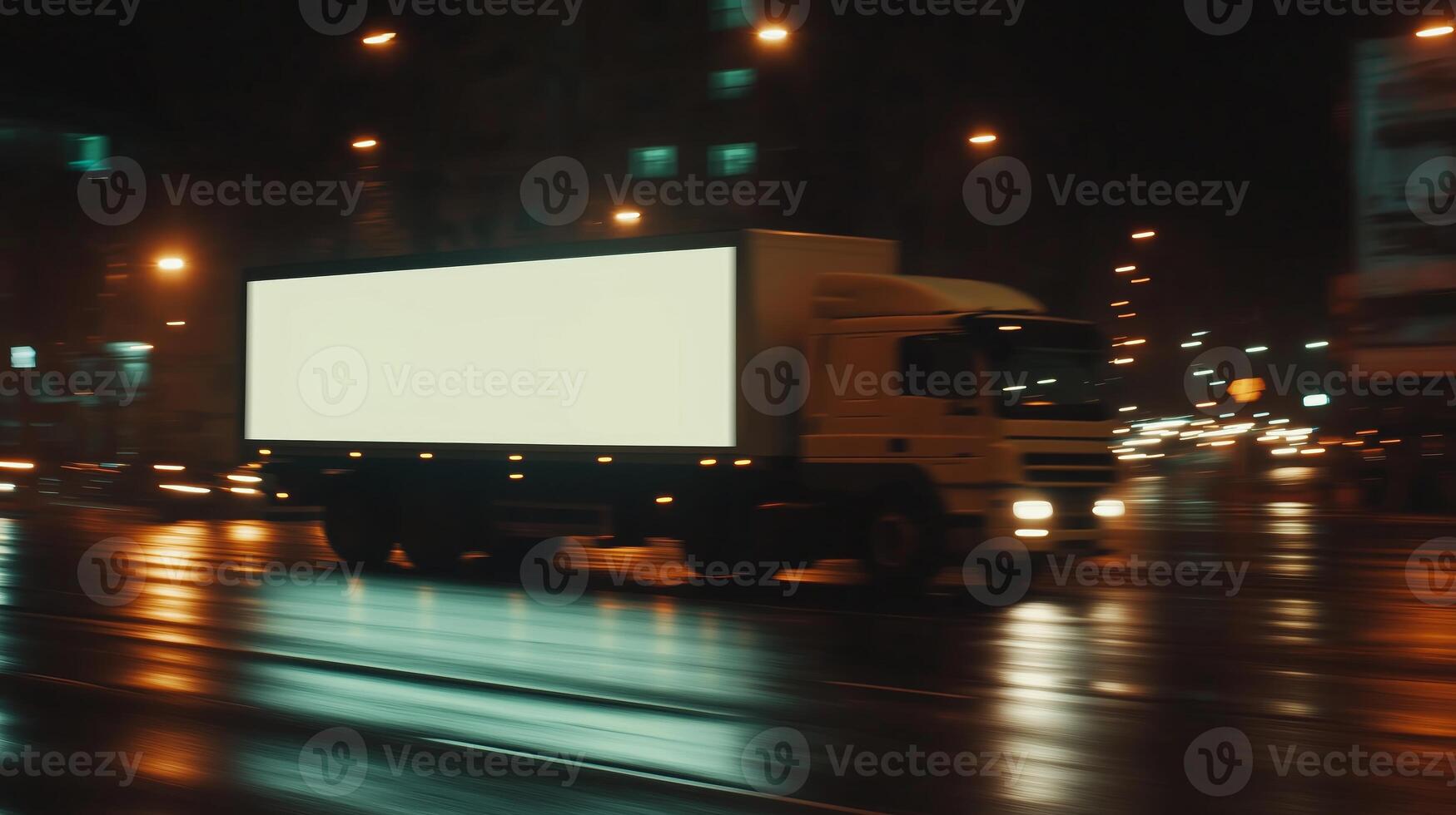 A truck driving down a street at night with a billboard on the back photo