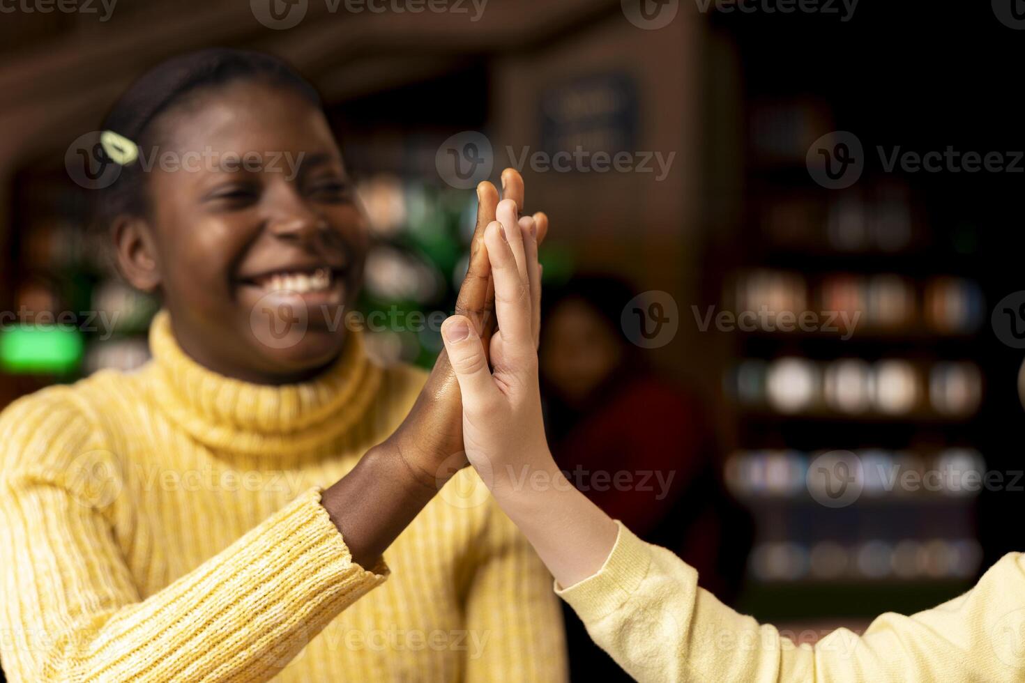 Confident diverse friends having fun and sharing a high five in the library, being proud of their finished school assignment. Happy adorable teen girls with a beautiful friendship. Close up. photo