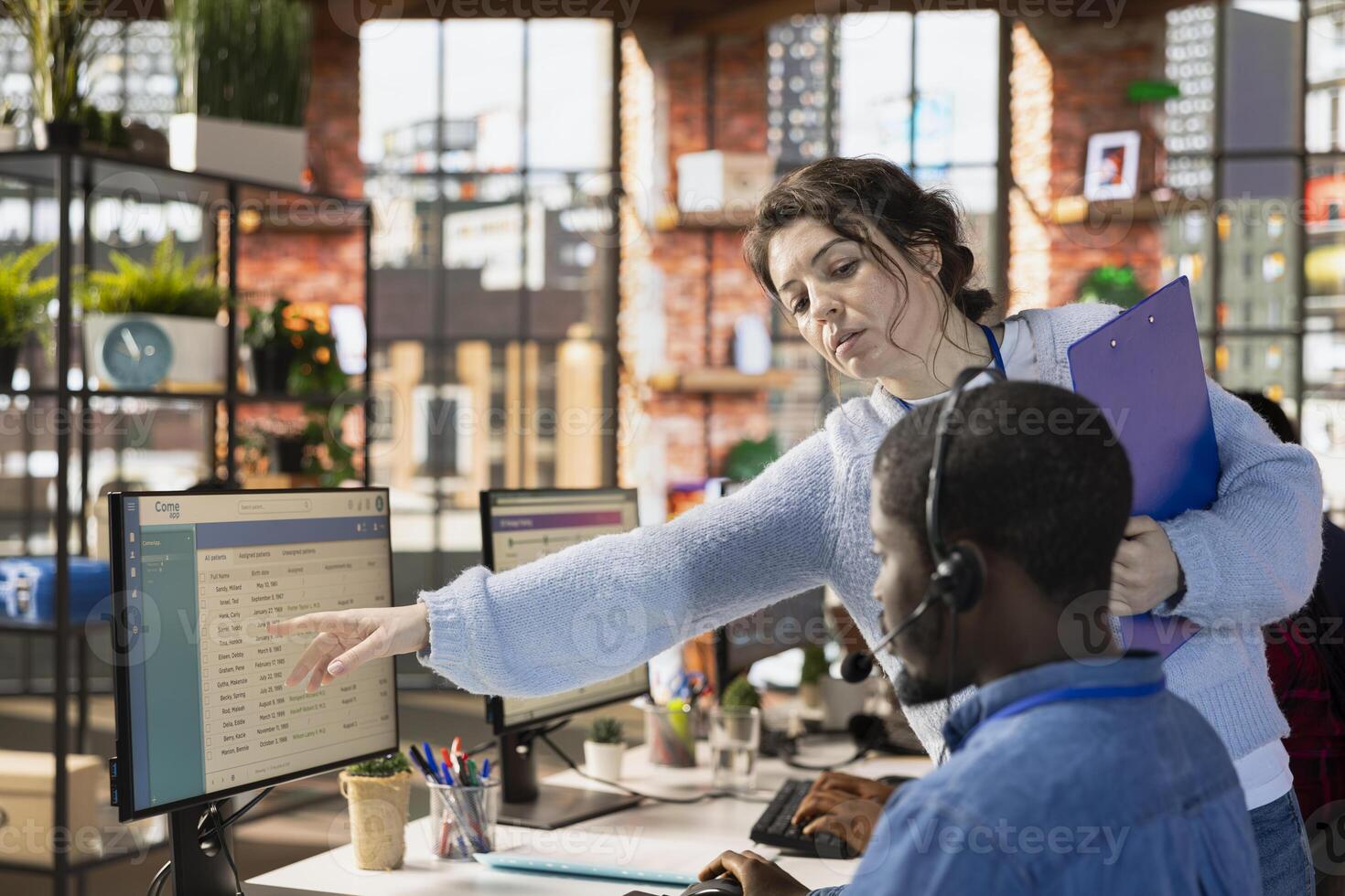 Customer center manager teaching man how to log customer interactions in CSM system on computer. Call center onboarding specialist tutoring intern on using customer service management software photo