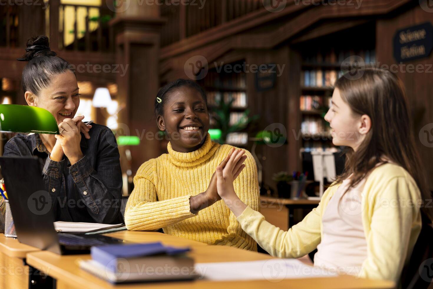Pleased happy schoolgirls sharing a high five during private lessons with tutor in the library, finishing their team project work. Elementary school pupils feeling satisfied with academic progress. photo