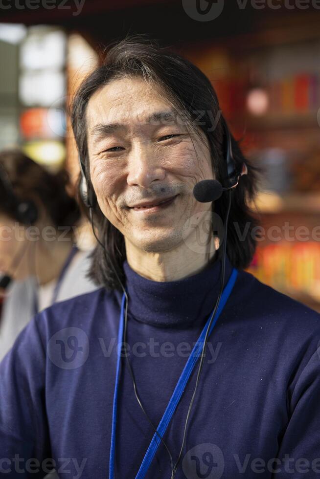 Portrait of cheerful senior call center agent dealing with unhappy customers, speaking with them using headset in office. Jolly experienced customer support representative handling clients complaints photo