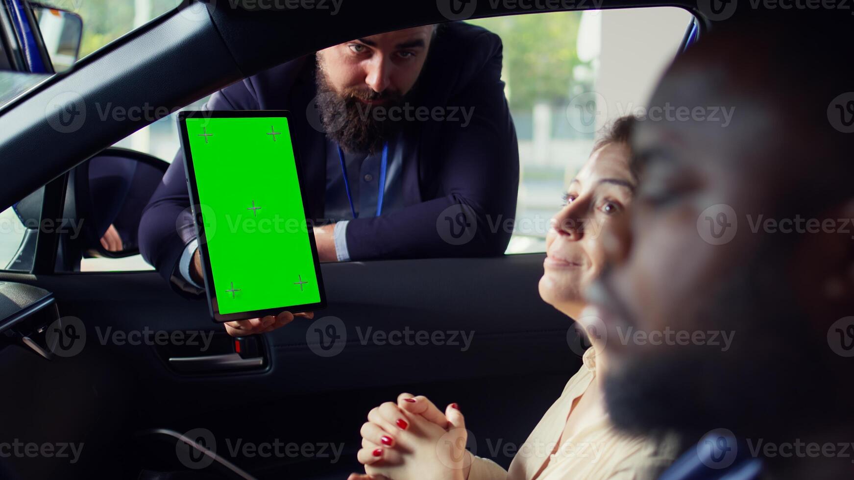 Showroom salesman showing stat charts on green screen tablet to clients after test drive. Dealership agent showing vehicle driving metrics graphs on chroma key device to couple, camera B photo