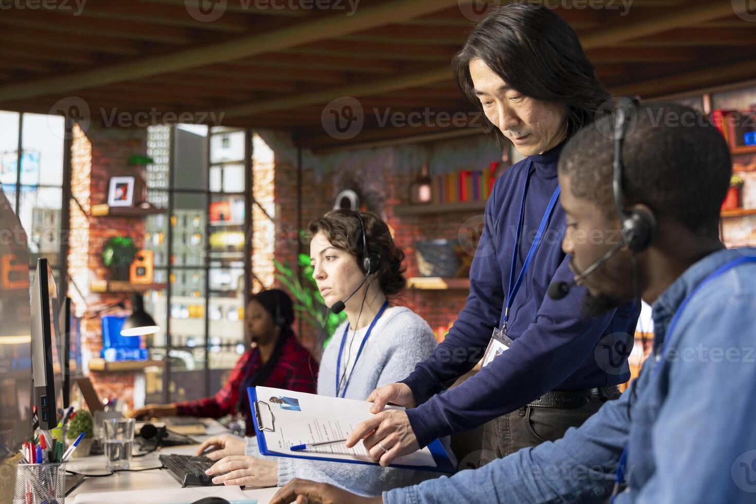 Call center senior manager going over job description file with employee at PC desk. Asian customer support onboarding specialist explaining tasks to intern accommodating with job photo