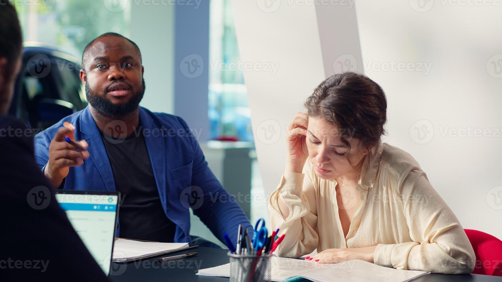 Customers negotiating correct price and financing options after finding right vehicle for them in showroom and deciding to buy it. Dealership clients reading contract terms and conditions, camera A photo