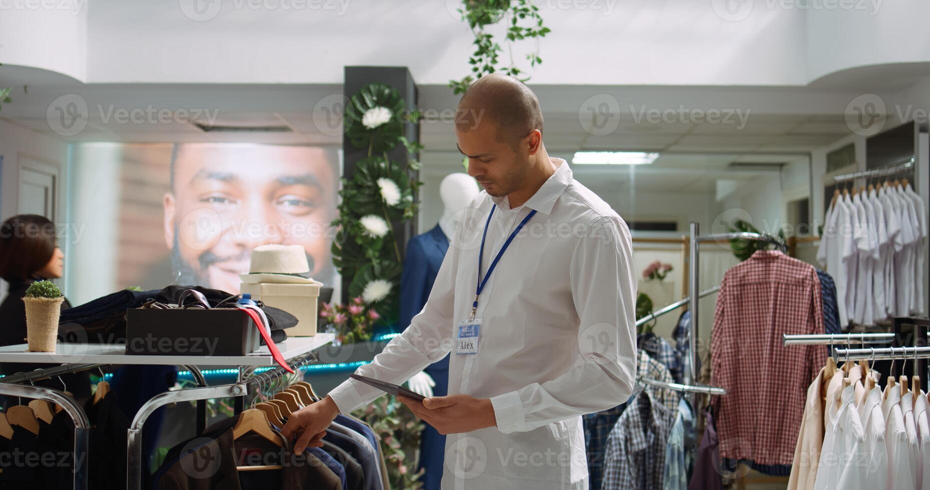 Middle eastern retail worker sorting new collection of merchandise on racks, arranging fashion items in a stylish mall store. Shop assistant showcasing attention to detail. Camera B. photo