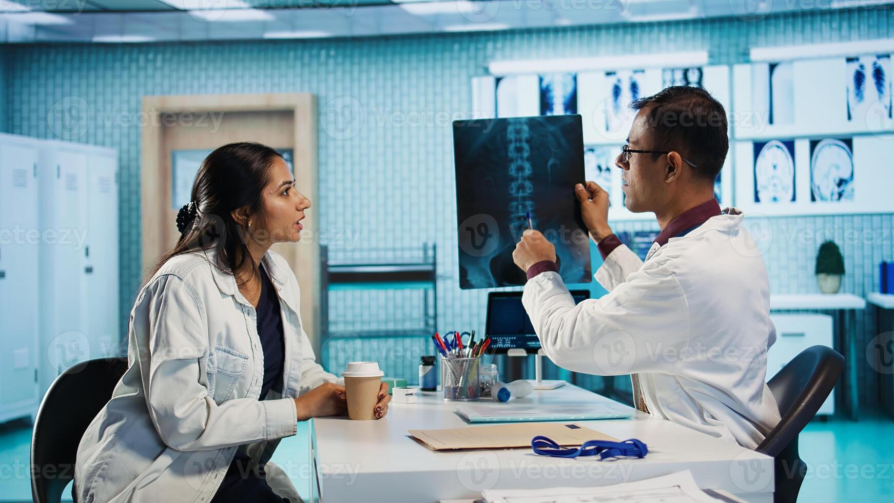 Professional medic and woman patient in a medical consultation looking at scans and MRI results, hospital records. General practitioner presents healthcare insurance to help with recovery. Camera B. photo