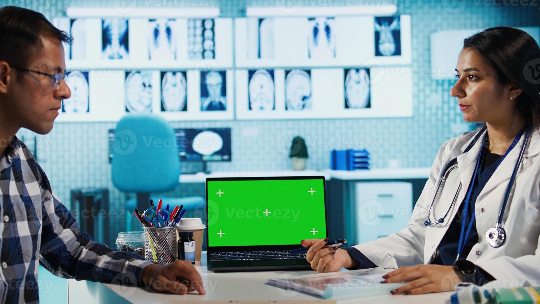 Indian physician consulting a patient in medical facility next to chroma key, using modern tech for scan interpretation and results. Medic giving professional advice based on records. Camera B. photo