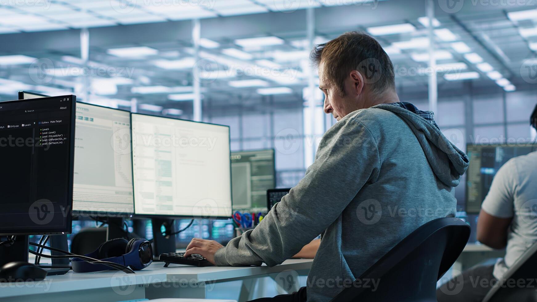 Fatigued admin stretching at work in server room to relieve muscle cramps while analyzing data on monitor. Tired man in data center relaxing body after overworking, camera A photo