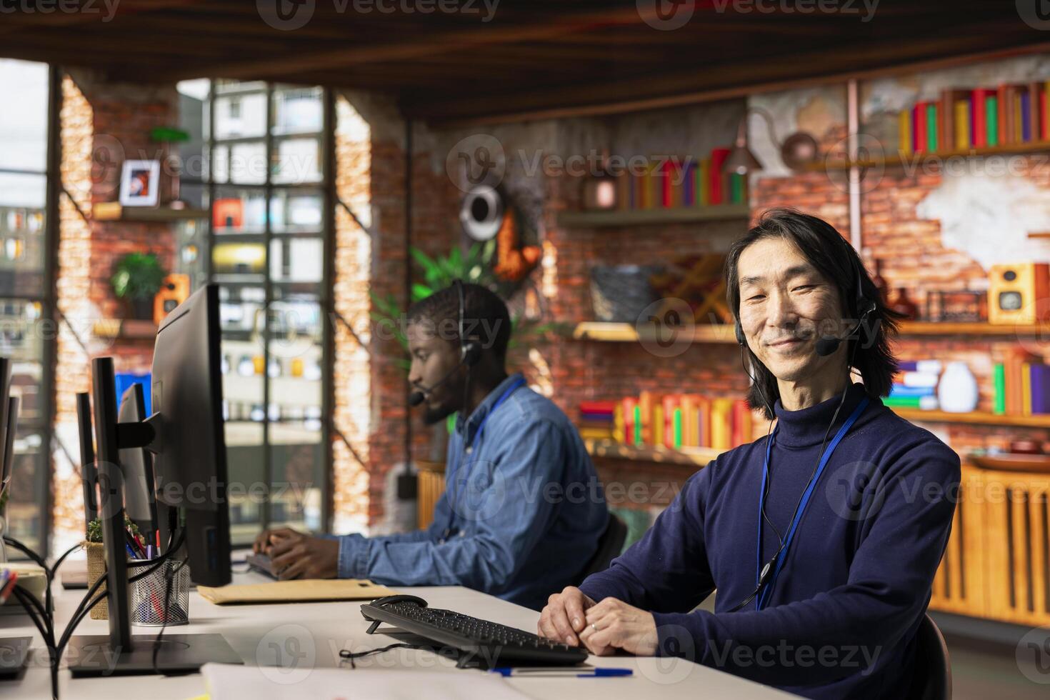 Portrait of cheerful call center agent using remote access tools on computer to connect to customer devices. Upbeat Asian customer center professional assisting clients with installing software photo
