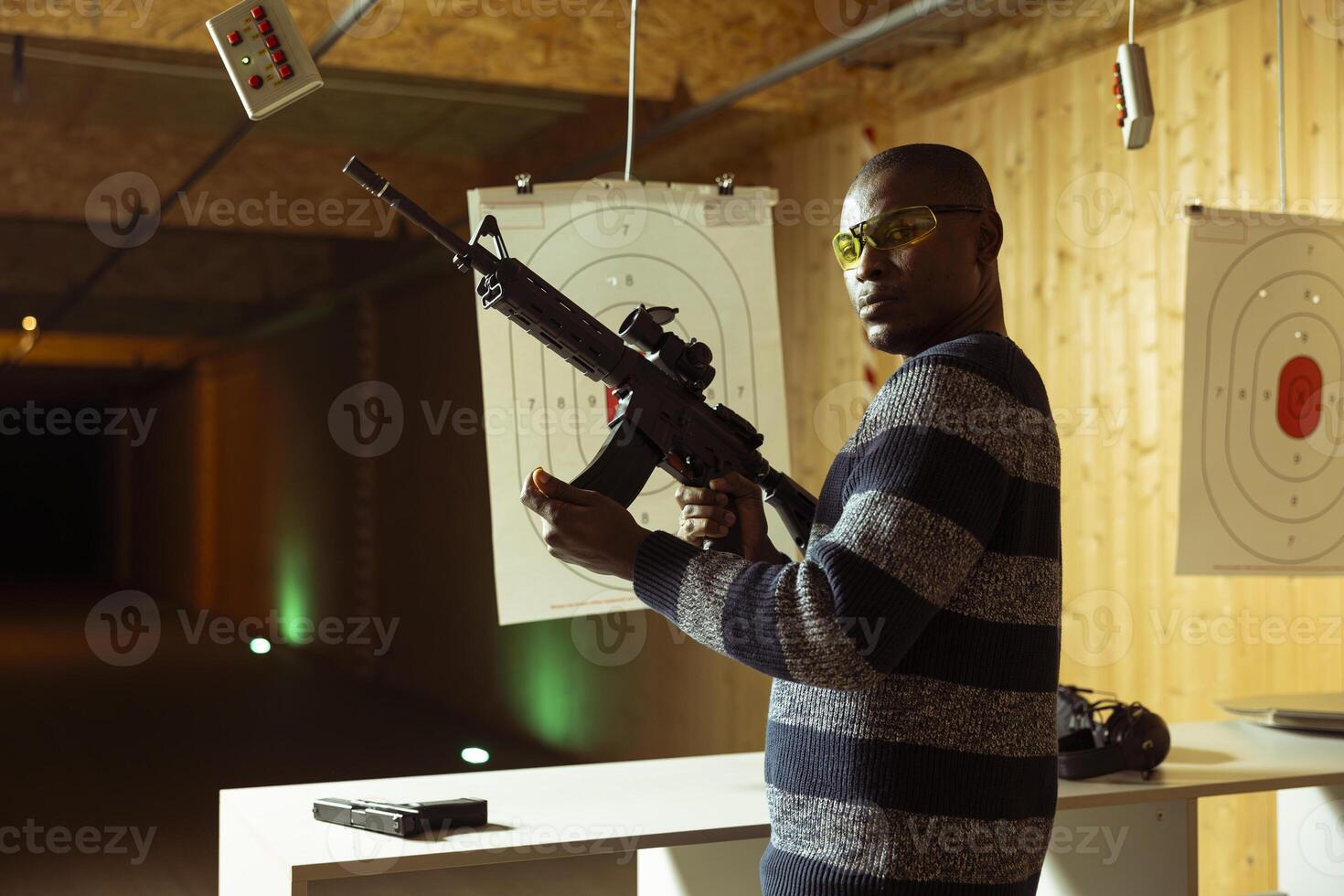 Portrait of shooting range client reloading rifle, preparing to shoot targets during leisure time. Man at indoor shooting ground facility loading semiautomatic weapon, wearing protection goggles photo