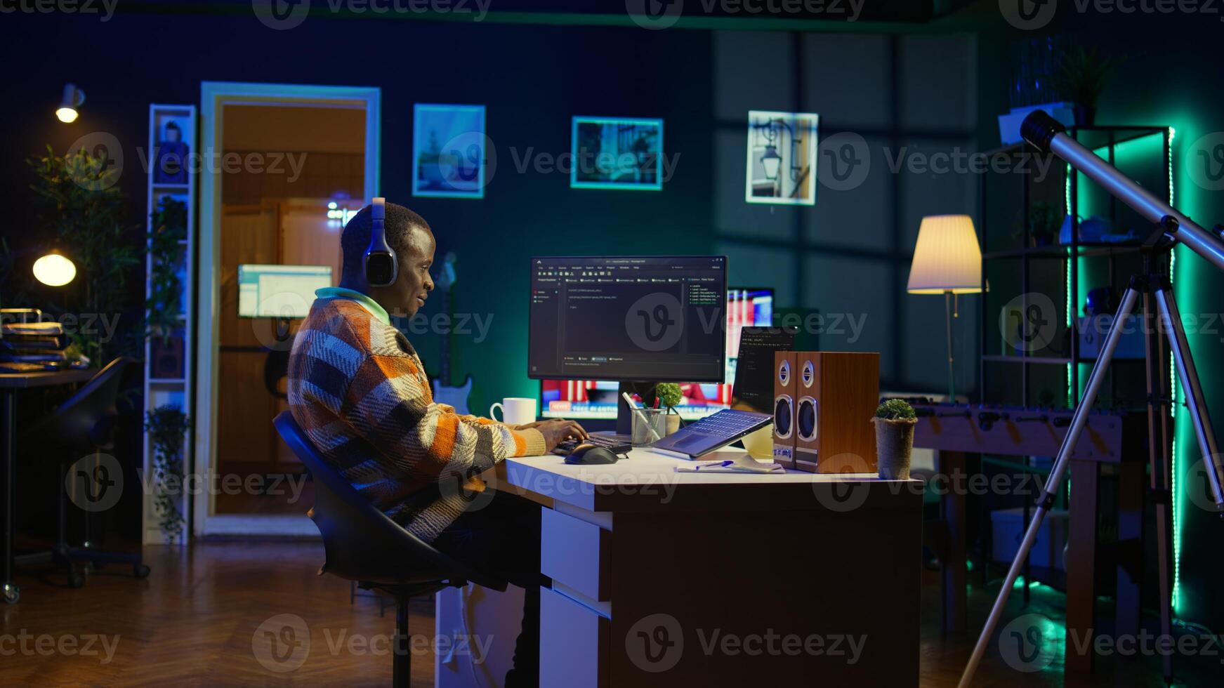 Black programmer remotely working in home office writing code on computer at his desk. Programming engineer IT expert in apartment typing lines of code at workstation, teleworking. Camera B. photo