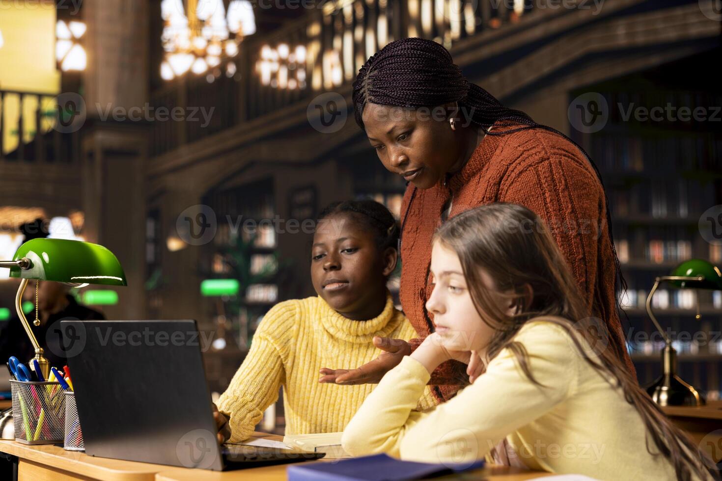 Two elementary school children working with a tutor practicing mathematics and developing their academic skills at a study desk. Black woman explains the curriculum materials to her pupils. photo