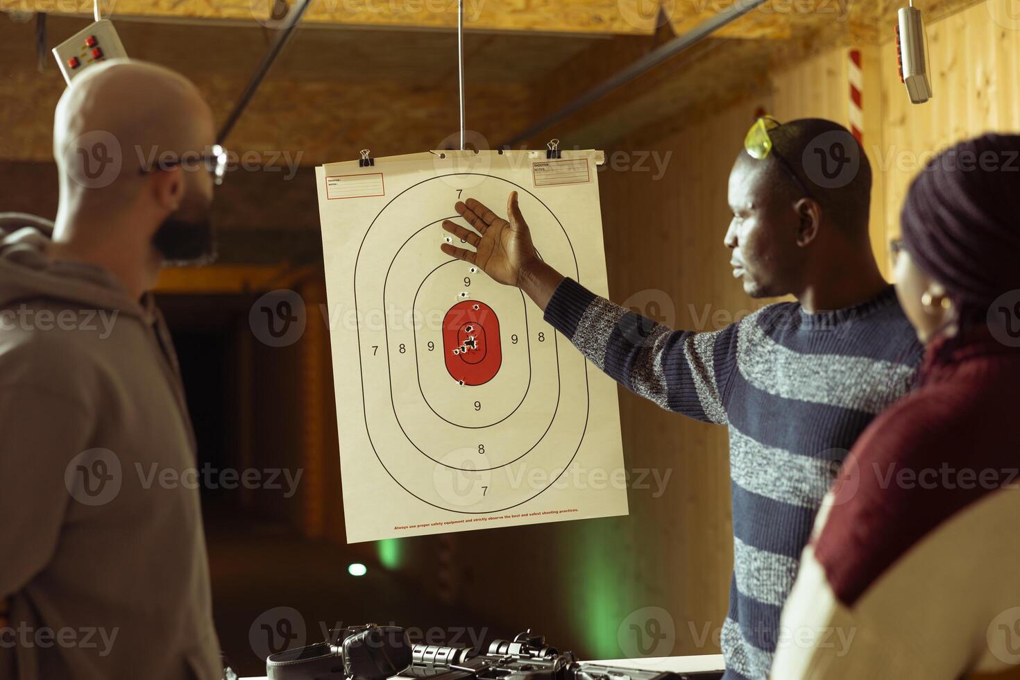 Group of friends having fun in shooting gallery, comparing results after hitting targets. Coworkers in teambuilding entertained by shooting bullseyes at firing range, doing competition photo