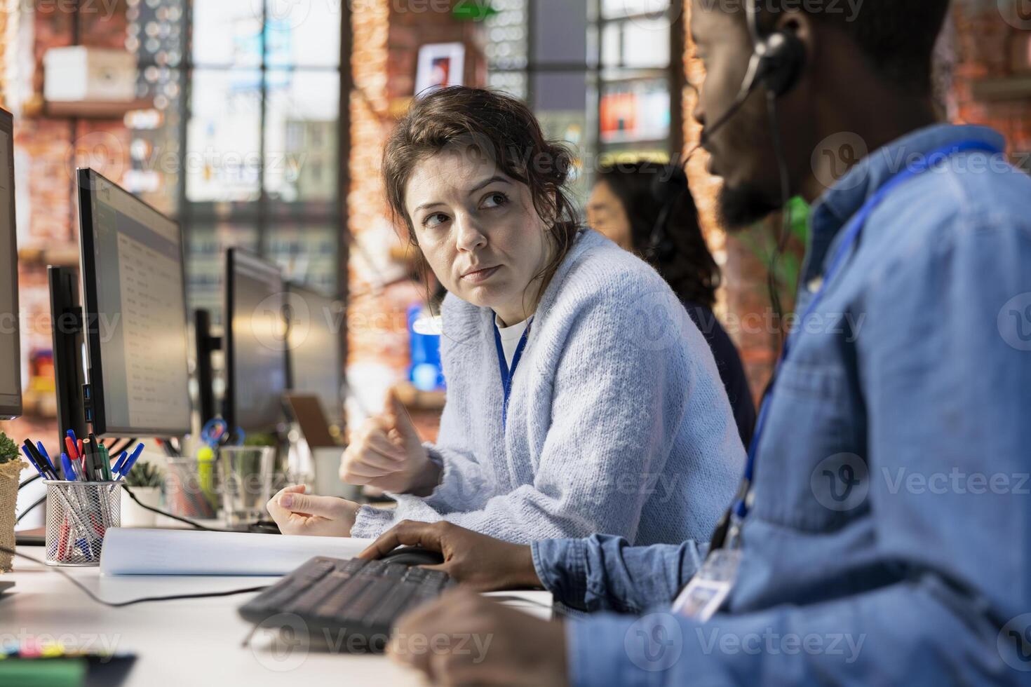 Customer service colleagues cooperating, logging customer interactions in CSM system on computer. Team of call center agents working together, using customer service management software on PC photo