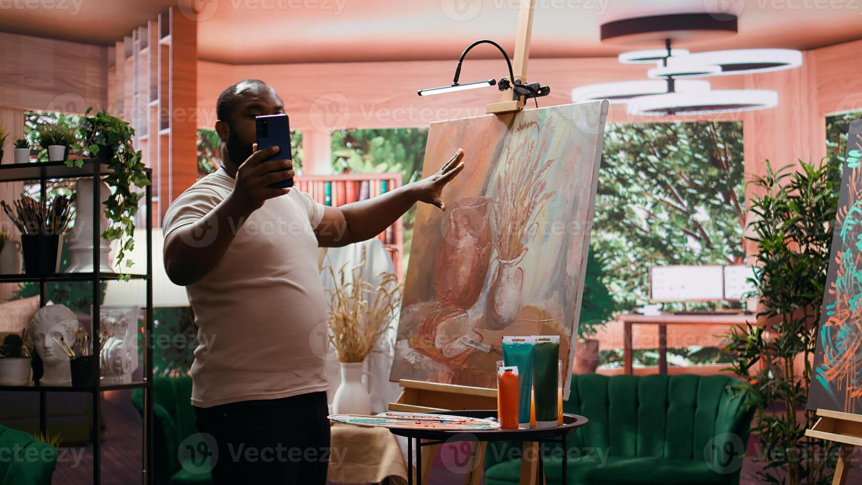 African american painter posting a picture of his masterpiece online on social media, building a better branding image for his content creation. Confident in self promotion. Camera B. photo