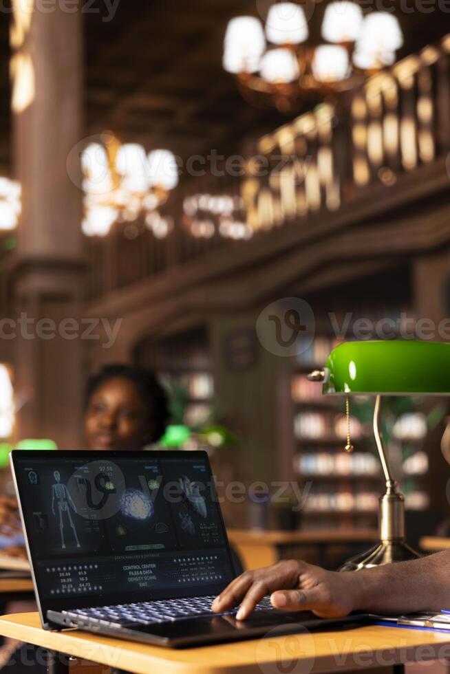 Med school student takes personal notes from anatomy research papers, studying healthcare methods for a medical career. African american pupil using books from the campus databases. photo