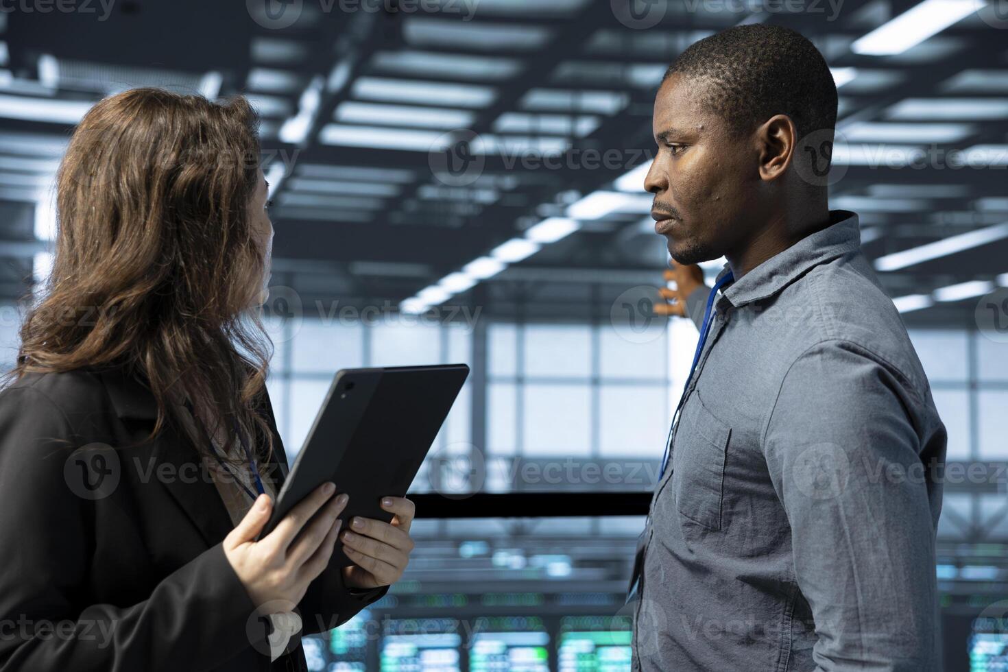 IT staff members in data center using tablet, verifying compliance requirements of rigs. Man and coworker in server room optimizing resource utilization, maintaining stable infrastructure using device photo