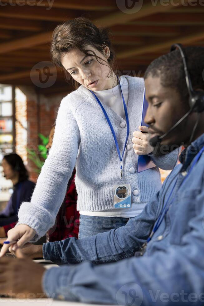 Call center manager providing guidance to african american intern, addressing questions. Customer service workplace onboarding specialist conducting orientation sessions for new agent, close up photo