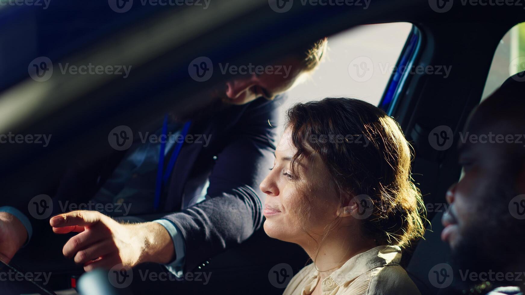 Showroom salesman showing purchasable extra car features on tablet to clients after they finished test drive. Dealership agent showing vehicle addons catalog to husband and wife on device, camera A photo