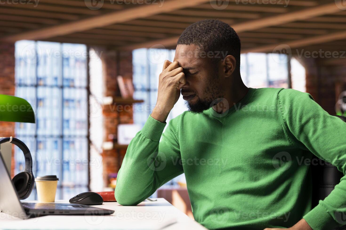 Man at home feeling exhausted and in pain from lack of sleep, suffering from insomnia fatigue. Exhausted African american person with negative emotion affected by ache, closing eyes, feeling stressed photo