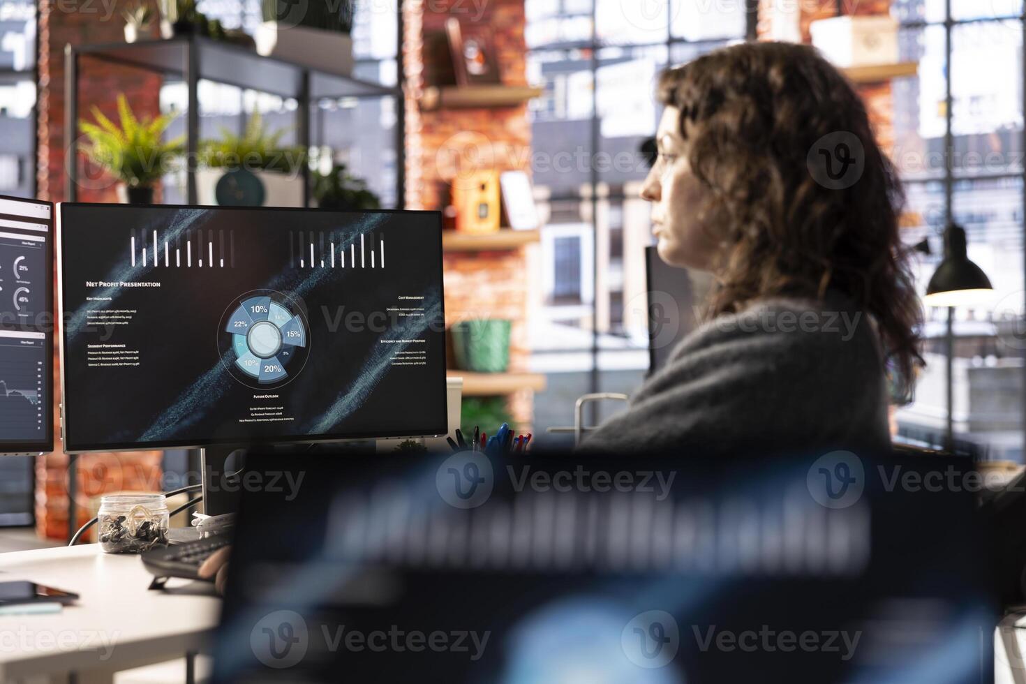 Young company analyst at office watching business presentation on PC display, reviewing statistics charts and performance metrics. Employee looking at presentation graphs on computer. photo